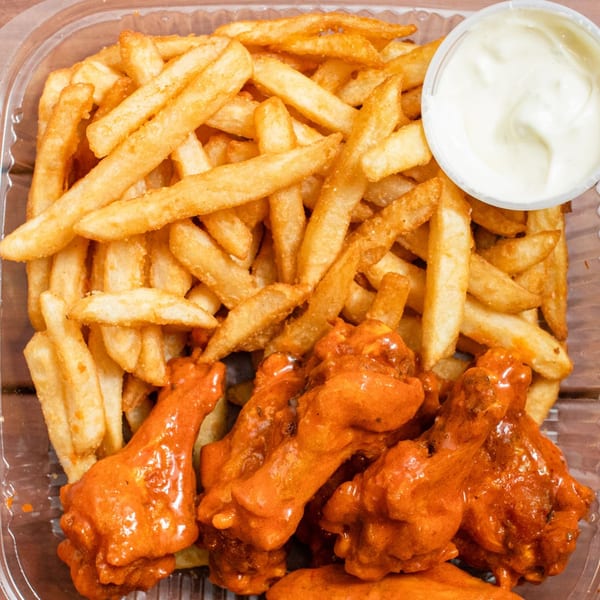 A takeout container filled with golden french fries, buffalo wings, and a side of ranch dressing.
