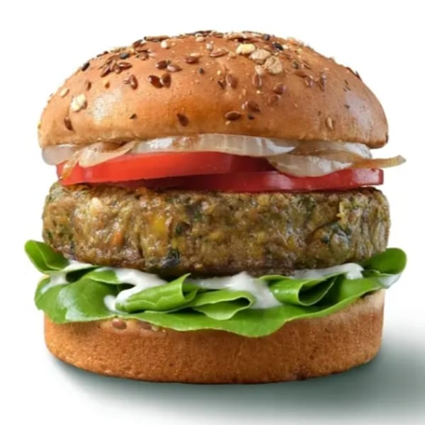 A veggie burger with lettuce, white sauce, a patty, tomato, and onions on a seeded bun.