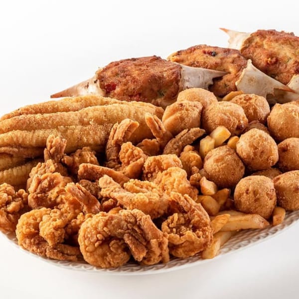 A large platter of fried seafood, including shrimp, fish, crab cakes, hush puppies, and french fries.